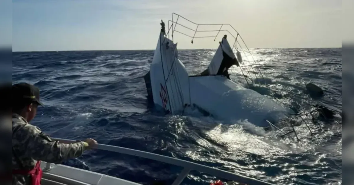 A small white boat partially submerged in rough open water; a rescue crew member on a nearby boat extends a line toward it.