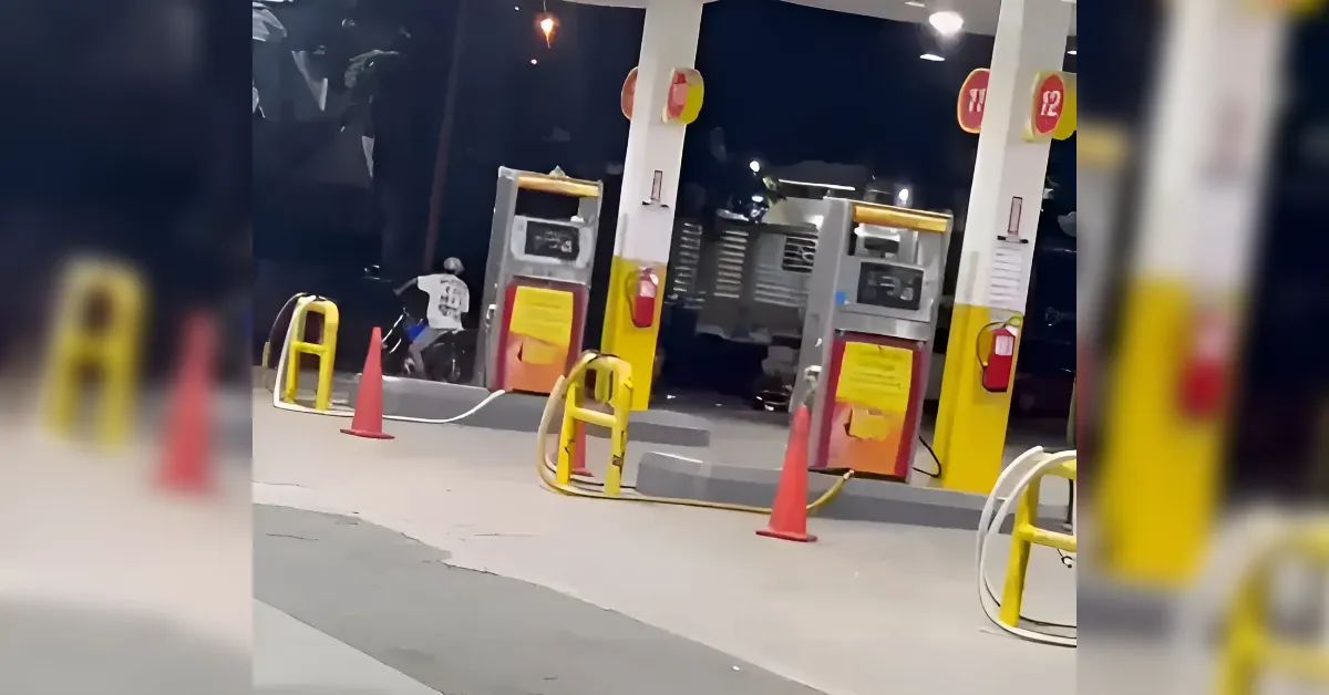 Gas station fueling island at night with two pumps, yellow safety posts, and orange traffic cones surrounding the area.