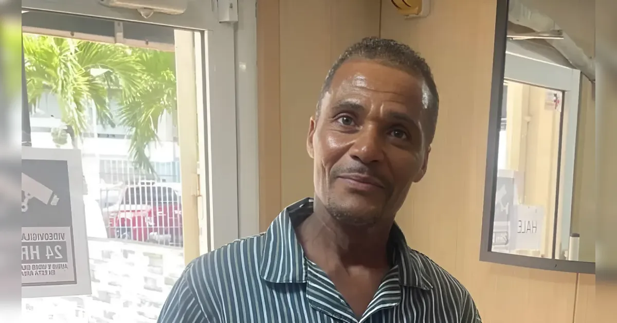 Man with short hair wearing a blue striped shirt smiles at the camera indoors.