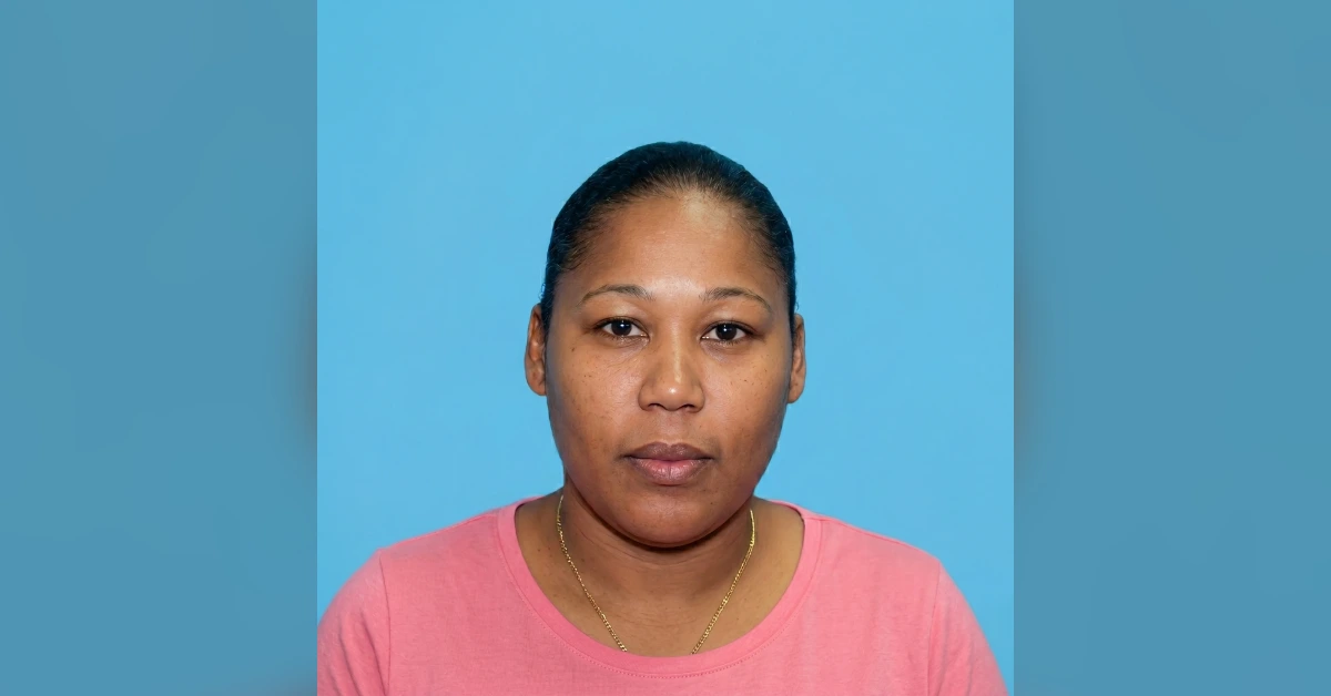 Portrait of a woman facing the camera, wearing a pink shirt and gold necklace, against a blue background.