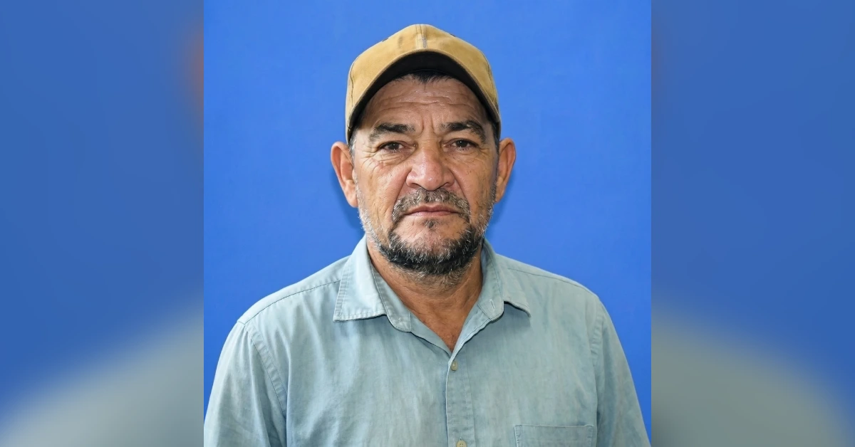 Portrait of a middle-aged man wearing a tan cap and light blue shirt against a solid blue background, looking at the camera.