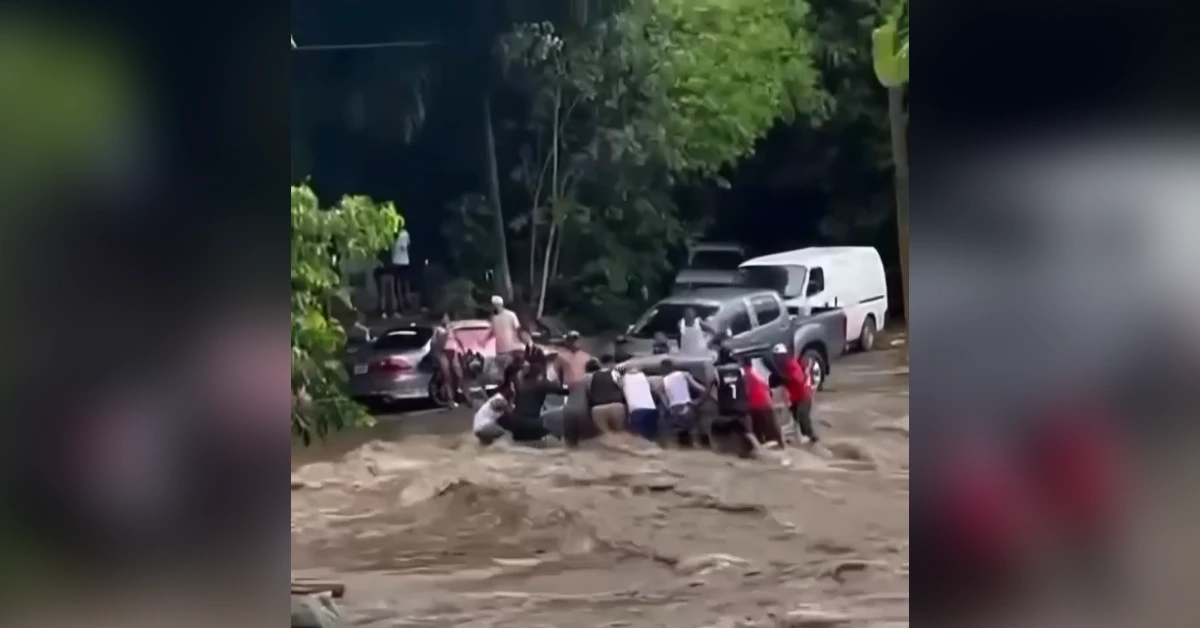 Group of people pushing a car through a flooded, muddy street as they work together to move it to higher ground.