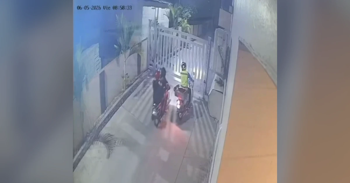 Surveillance still showing two people on motorcycles stopped at a closed gate at a driveway entrance, one rider wearing a reflective vest.