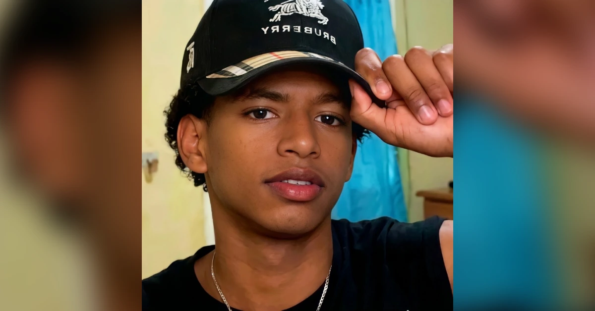 Young man wearing a black Burberry cap, touching the brim with his right hand, indoors in a casual pose
