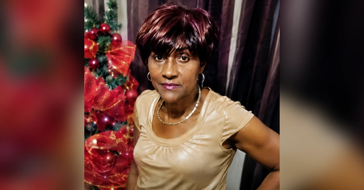 Portrait of a middle-aged woman with short burgundy hair, wearing a beige top and hoop earrings, standing beside a decorated Christmas tree.