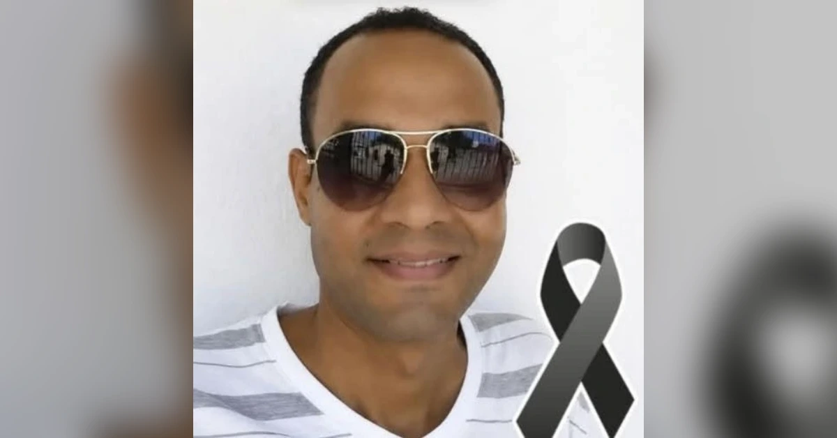 Smiling man in sunglasses wearing a white striped shirt, with a black mourning ribbon beside him.