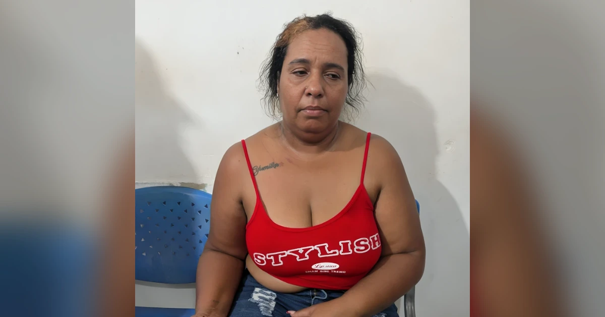 Woman seated on a blue chair, wearing a red sleeveless top with white lettering, looking downward.