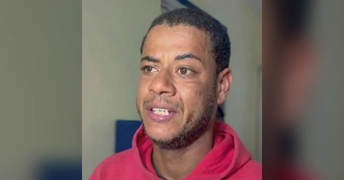 Close-up of a man with short hair and stubble wearing a red hoodie, looking to the left.