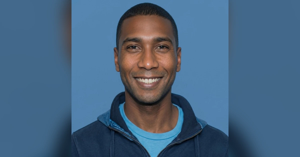 Smiling man in a blue hoodie and light blue shirt, head-and-shoulders portrait against a blue background.