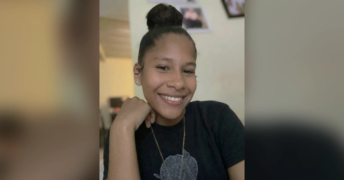 Smiling young woman with her hair in a top bun, resting her chin on her hand indoors