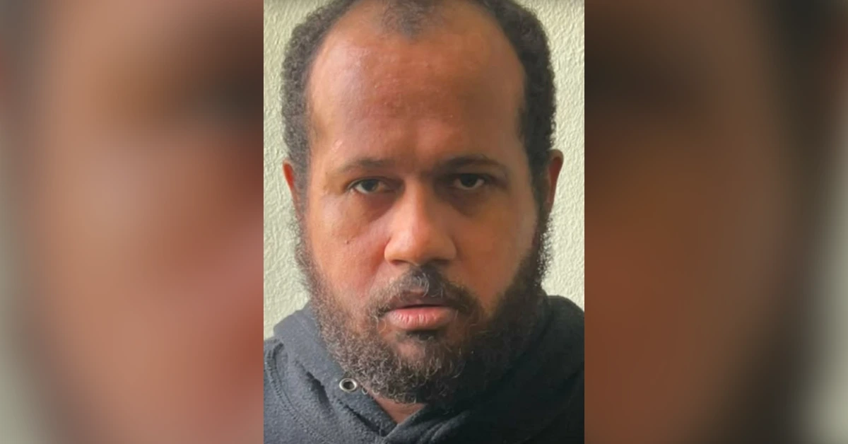 Close-up of a man with a beard and receding hairline looking at the camera, wearing a dark hoodie against a neutral background.