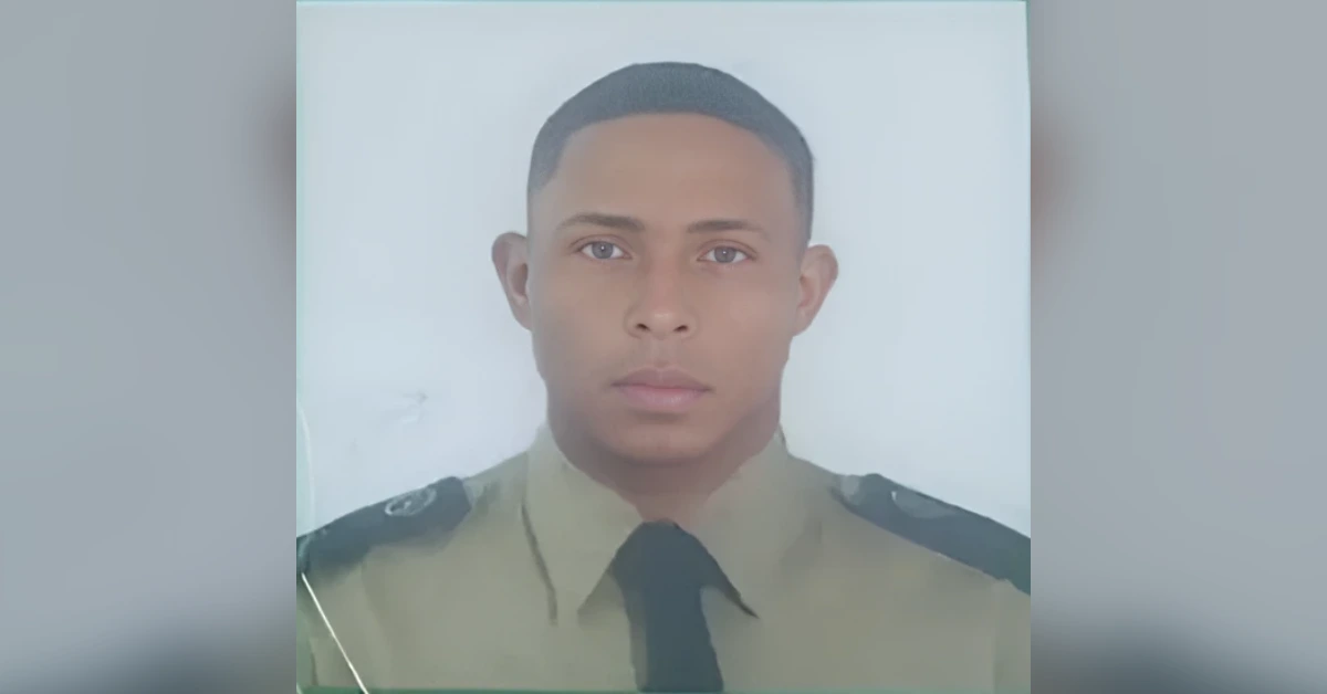 Portrait of a young man in a tan military uniform with a black tie, looking straight at the camera with a neutral expression.