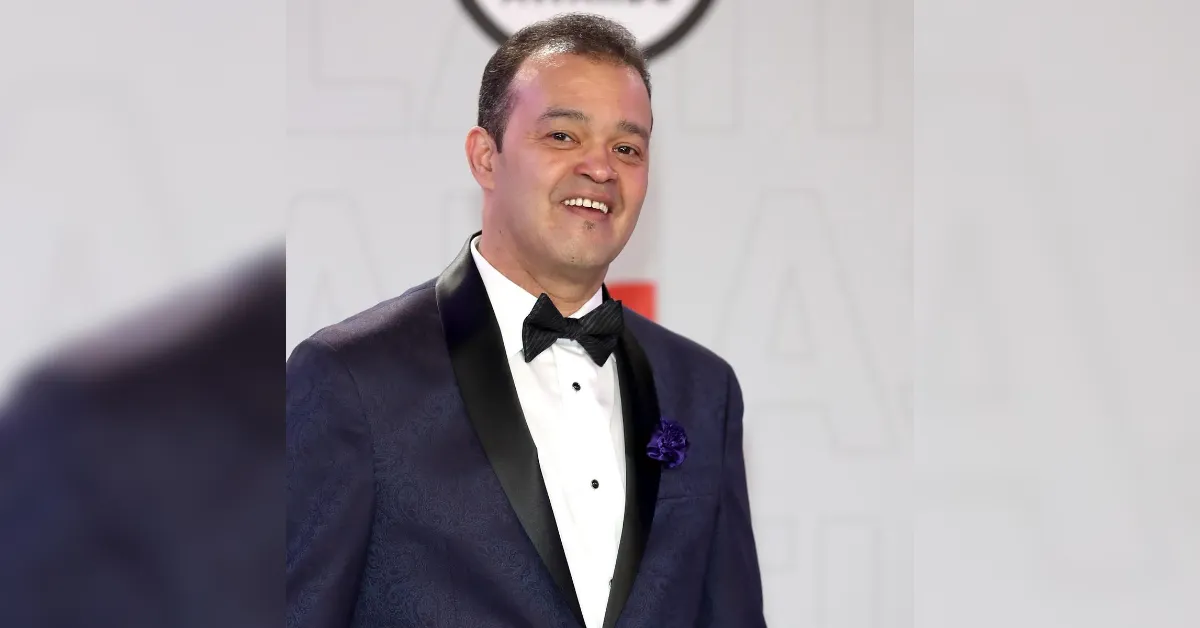 Man in a navy tuxedo with a bow tie, smiling on a formal red-carpet event.