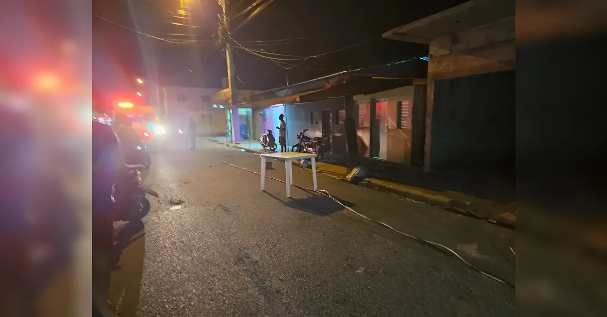 Nighttime street scene with red emergency lights on the left, a white plastic table in the road, and motorcycles parked along the curb.