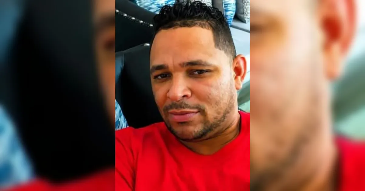 Close-up portrait of a man taking a selfie, wearing a red shirt with short dark hair and facial hair.