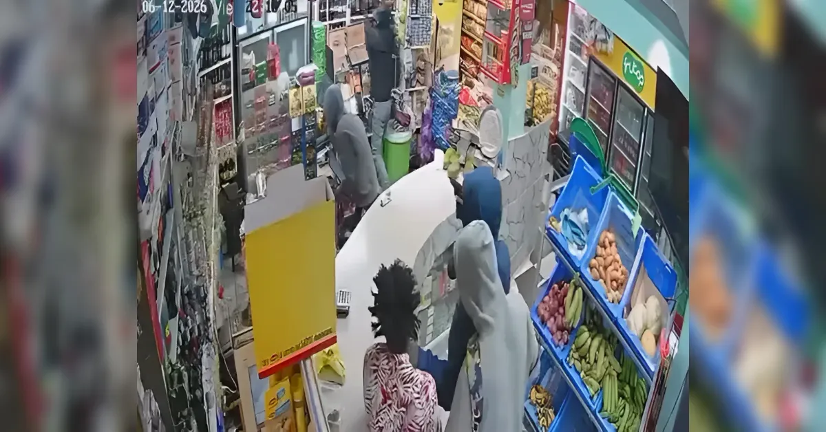 CCTV-style footage of a bustling shop with customers at a counter and fruit displays on the right side, shelves full of items in the background.