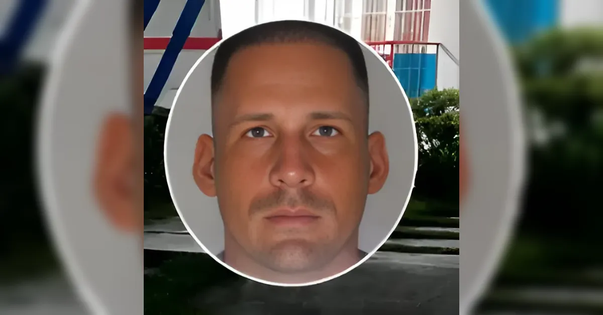 Close-up portrait of a man with short hair and a light mustache, framed by a white circular outline against a blurred outdoor background.