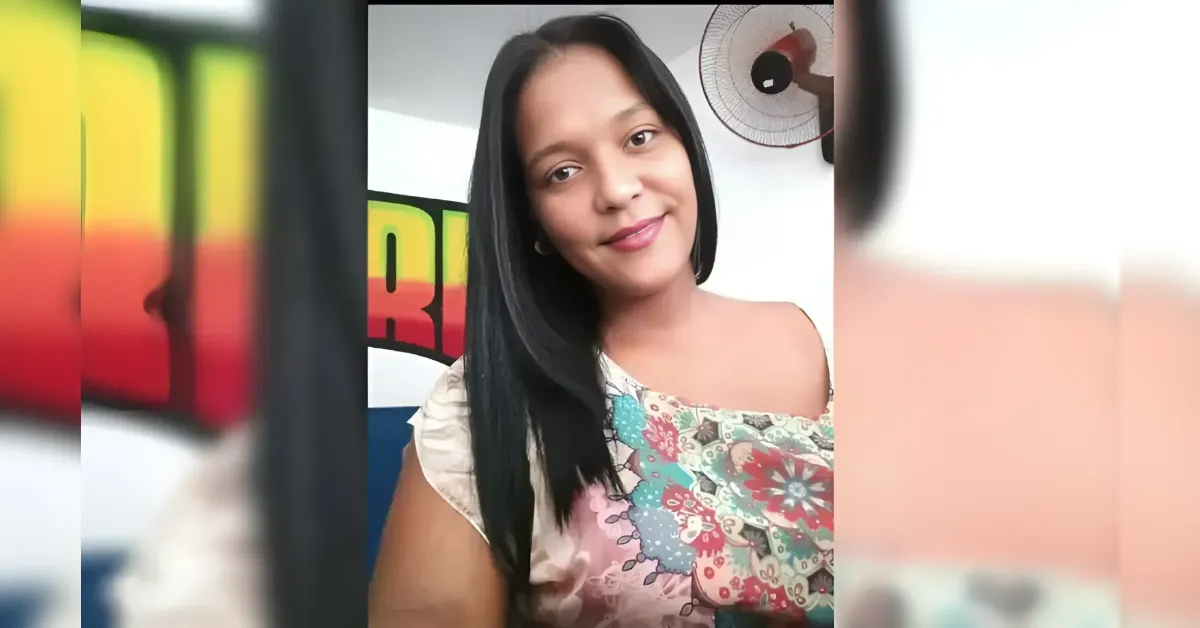 Smiling woman with long black hair wearing a floral off-the-shoulder top, posing for a selfie indoors.
