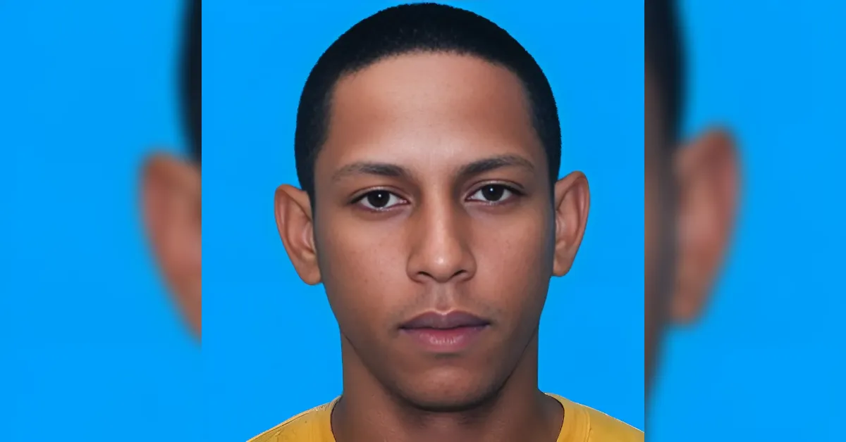 Close-up portrait of a young man with short black hair against a bright blue background, wearing a yellow shirt.