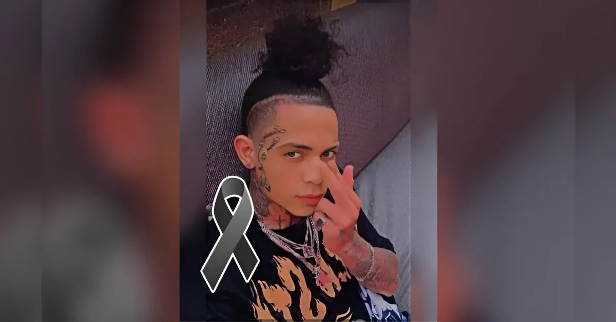 Portrait of a tattooed person with a top knot, wearing a flame-pattern shirt and silver chains, touching their face with a black ribbon overlay