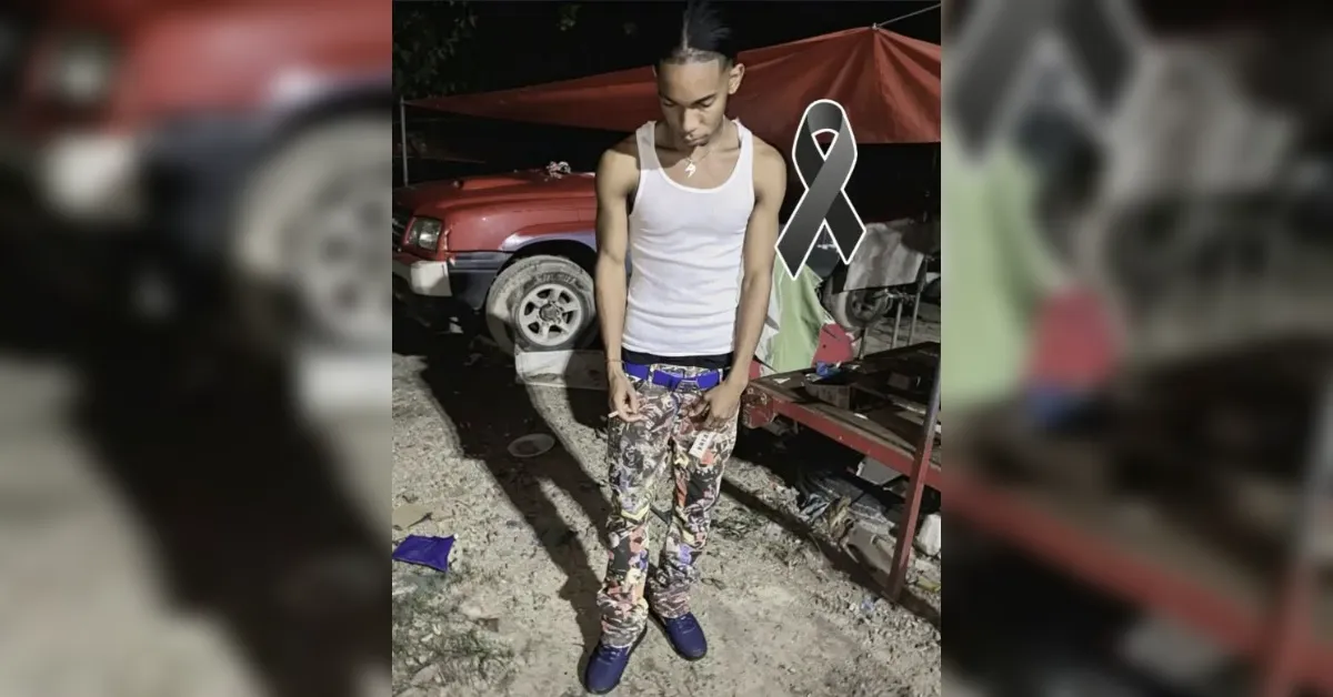 Young man in a white tank top and patterned pants stands on gravel at night near a red vehicle, with a gray ribbon graphic overlaid.
