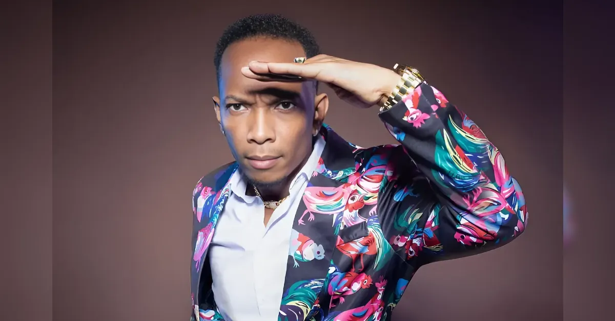 Portrait of a man in a vibrant, floral blazer saluting with his right hand, looking ahead against a brown gradient background.