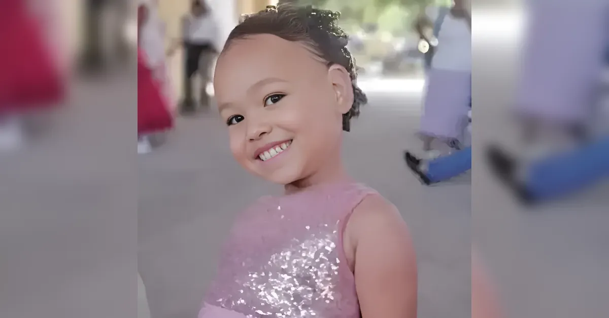 Little girl in a pink sequin dress smiles at the camera outdoors.