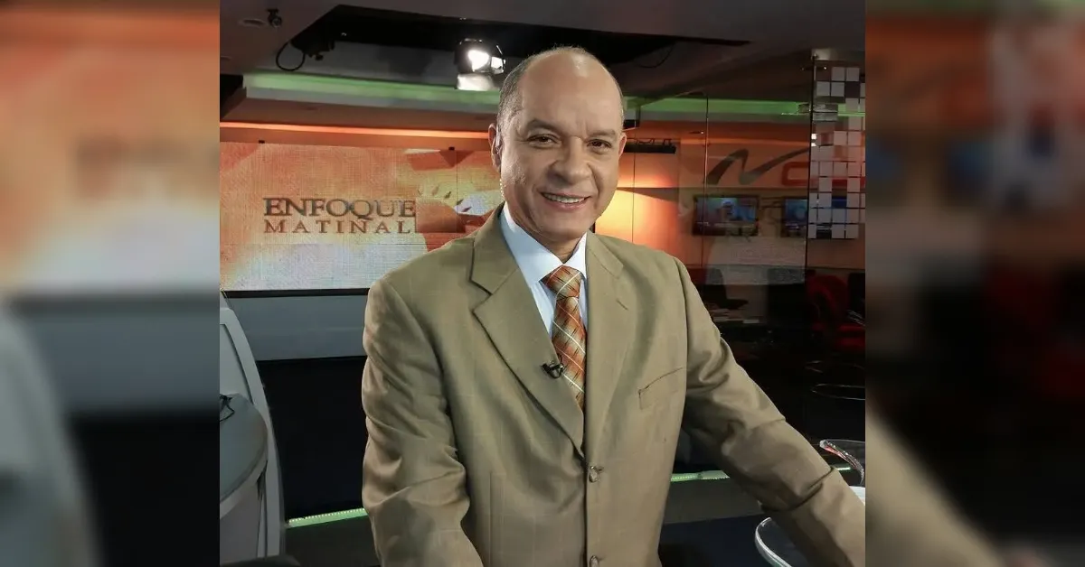 Smiling male news anchor in a beige suit in a television studio with 'Enfoque Matinal' signage in the background.