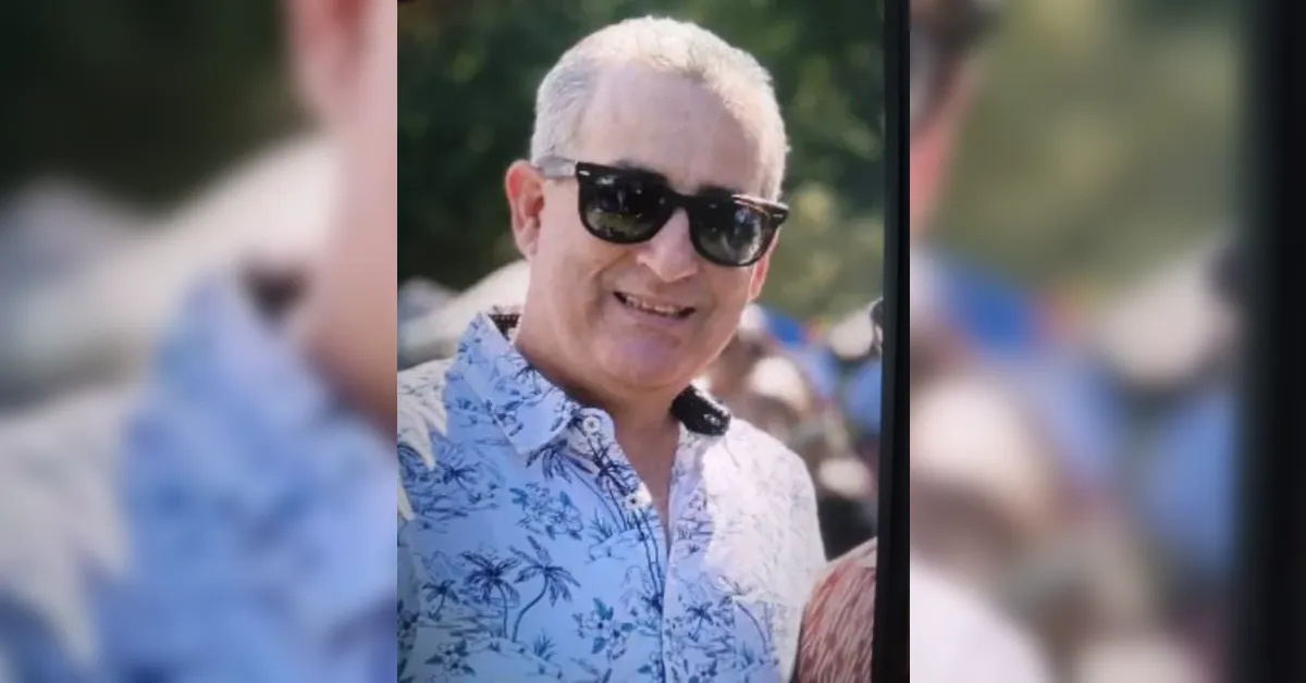 Smiling man in a blue floral shirt and black sunglasses at an outdoor event.