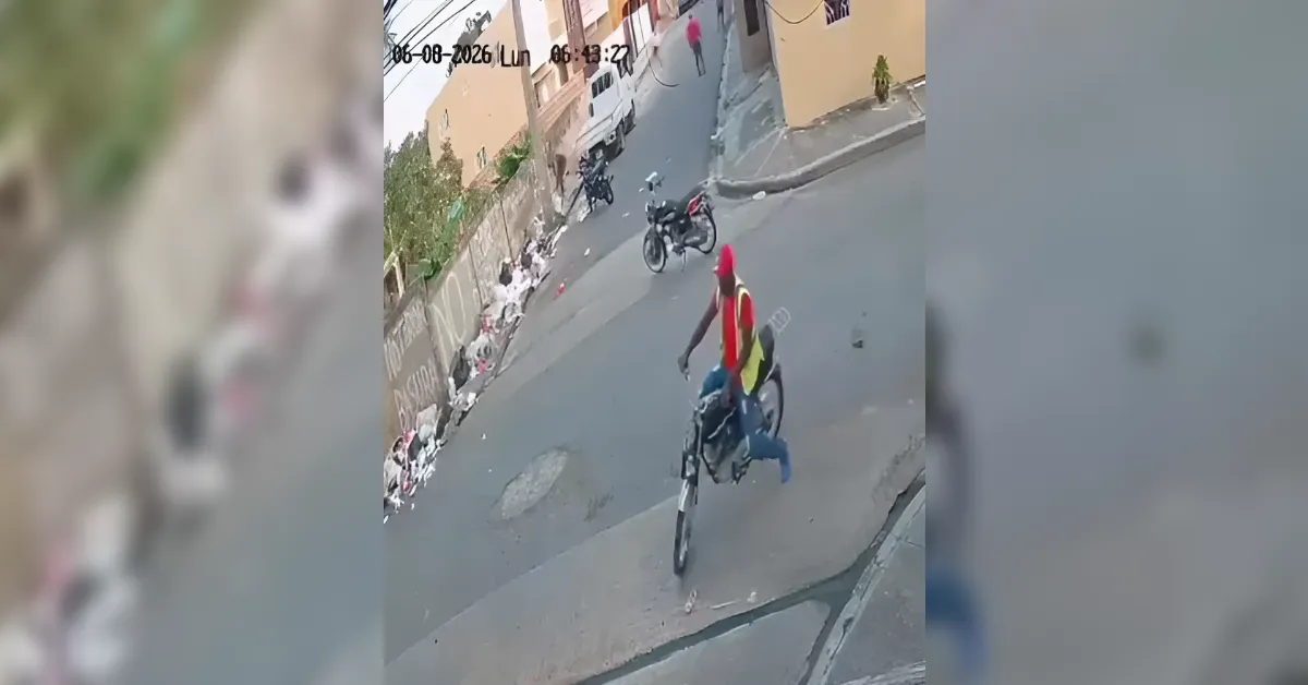 Surveillance shot of two people on a motorcycle on a sloped urban street, with piles of trash along the sidewalk and beige buildings in the background.
