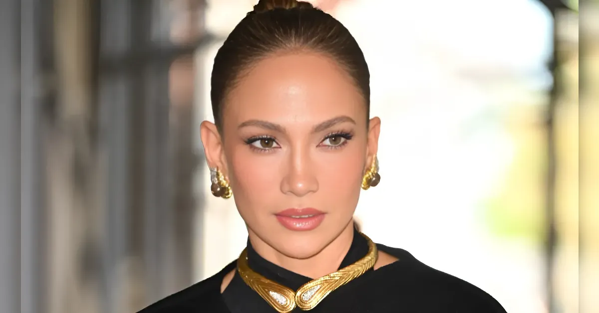 Portrait of a woman with slicked-back hair, gold statement earrings, and a matching gold choker against a blurred background.