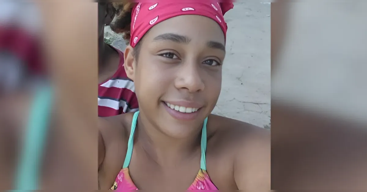 Smiling young woman taking a selfie at the beach, wearing a pink bandana and turquoise swimsuit straps.