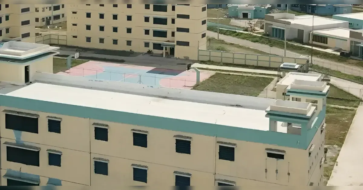 Aerial view of beige apartment buildings with teal trim, showing a pastel-colored courtyard and surrounding streets.