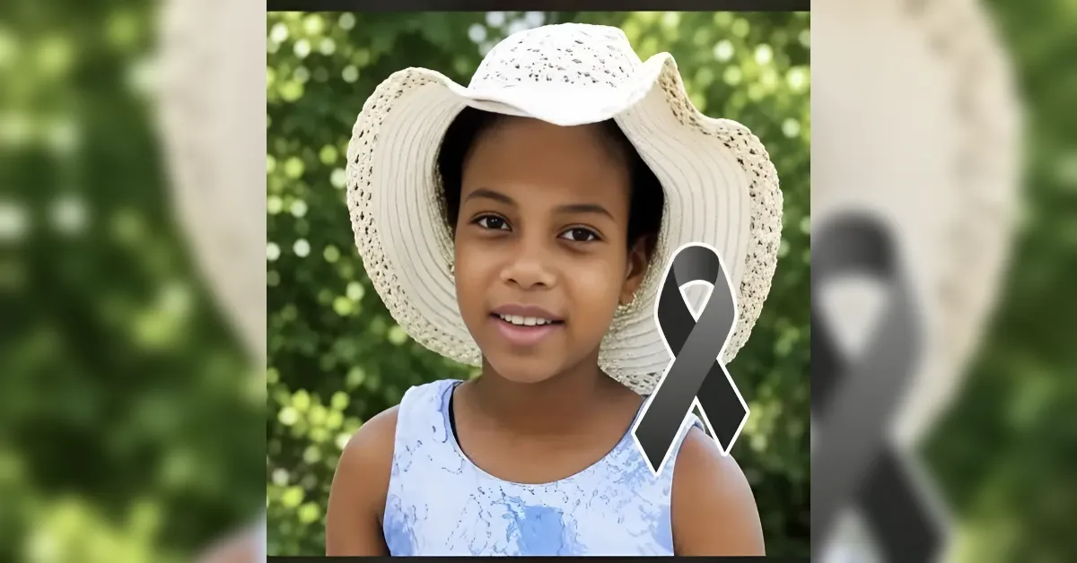 Girl with a wide-brim straw hat outdoors, smiling, with a black memorial ribbon overlay on the image.