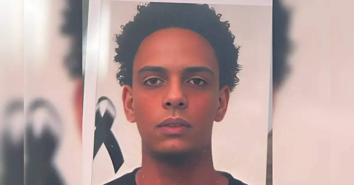 Portrait of a young man with short curly hair looking at the camera; a black ribbon appears in the background, suggesting mourning.