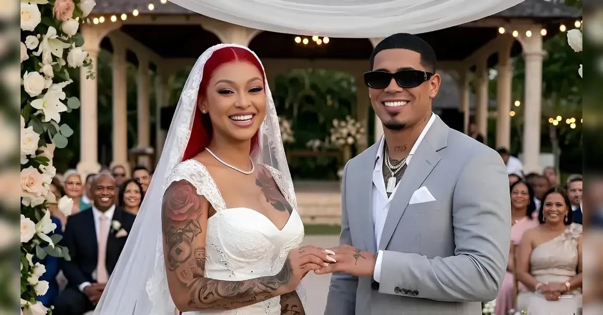 Bride and groom exchanging rings at an outdoor wedding under a floral arch; bride in lace gown with veil, groom in a gray suit and sunglasses.