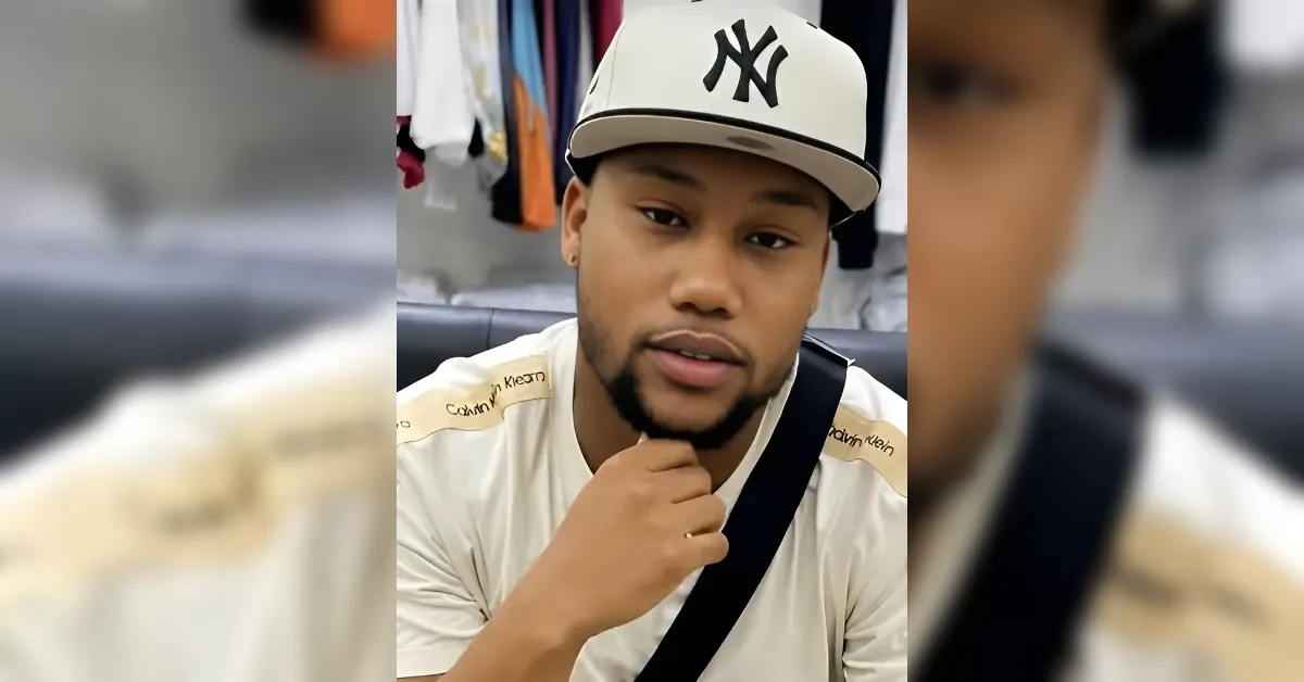 Portrait of a man wearing a white cap with a black NY logo and a beige Calvin Klein shirt, looking at the camera in a casual setting.