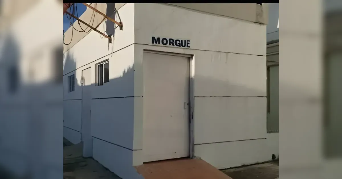 White, windowed building with a metal door; the word 'MORGUE' is painted above the entrance, indicating a morgue facility exterior.