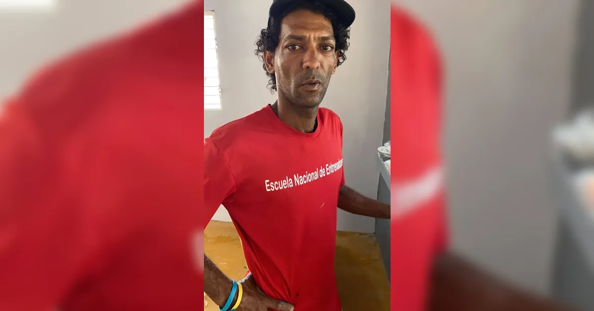 Man in a red T-shirt with white text, standing indoors and looking at the camera, wearing a dark cap.