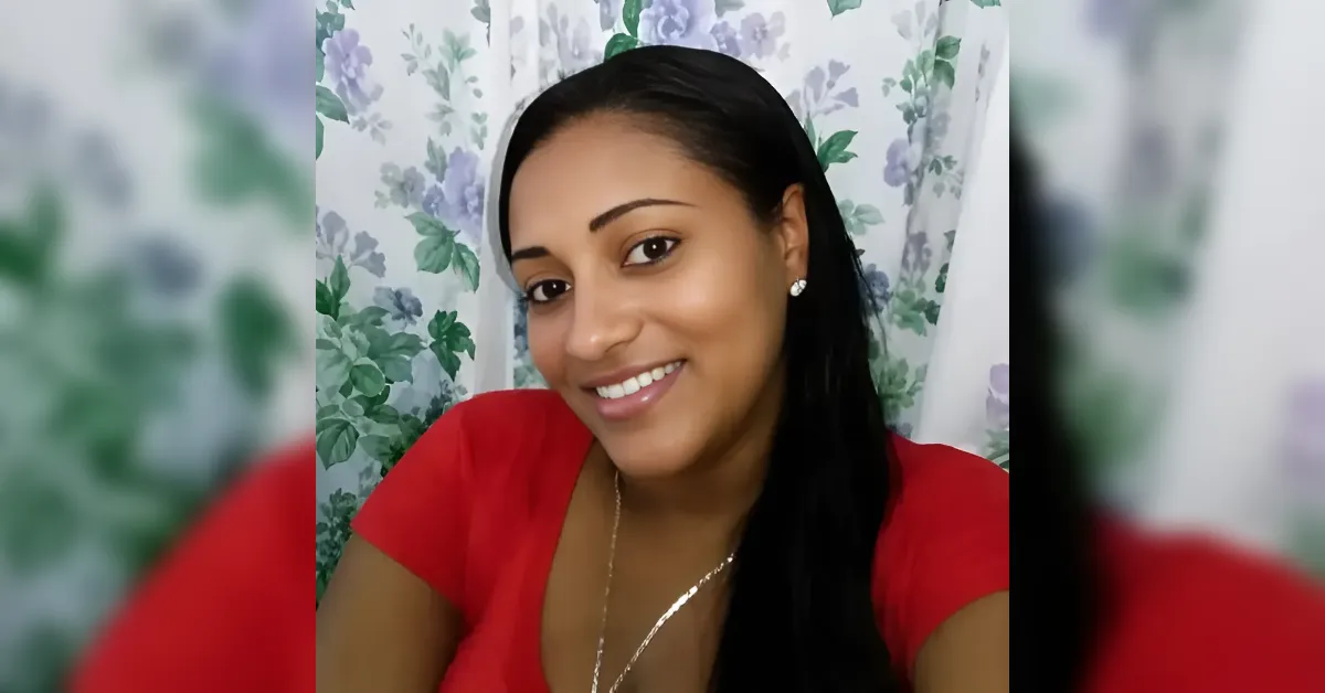 Smiling woman with long dark hair wearing a red top, posing in front of a floral curtain backdrop.