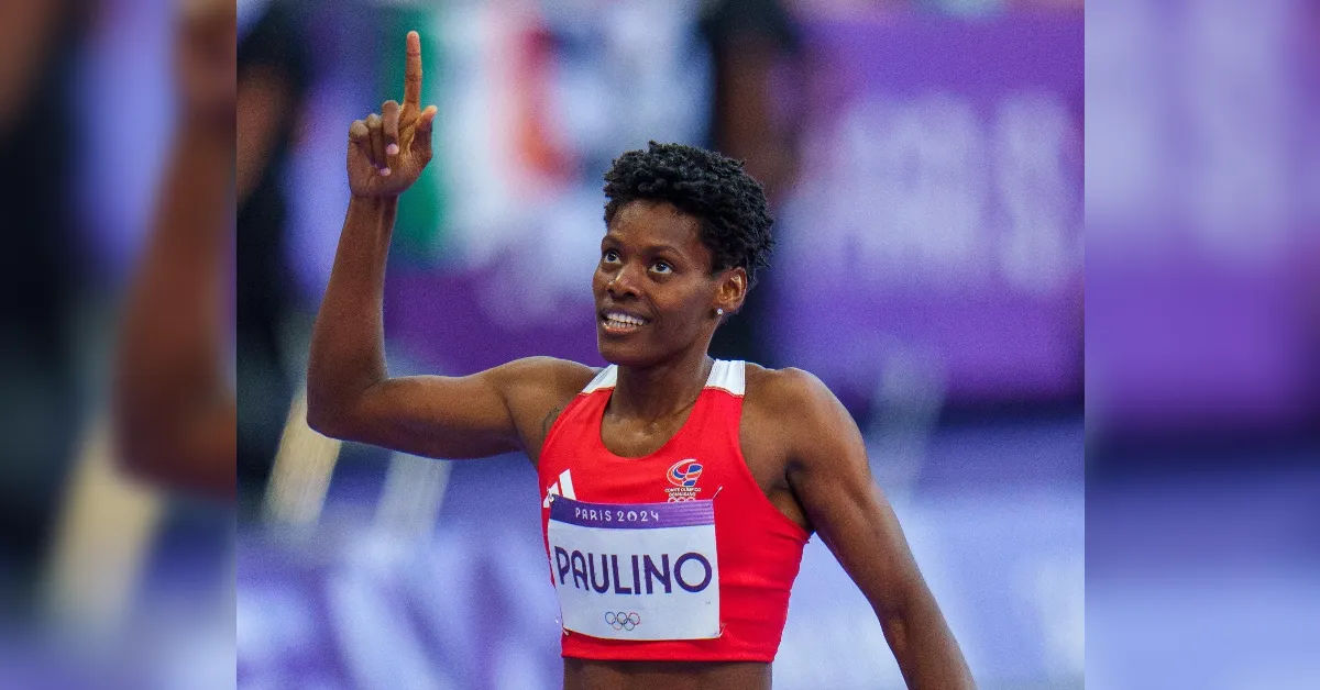 Female sprinter in a red top celebrates on the track, raising her index finger, with PAULINO on her Paris 2024 bib.