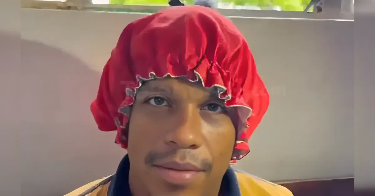 Close-up of a man wearing a red shower cap, looking at the camera indoors.