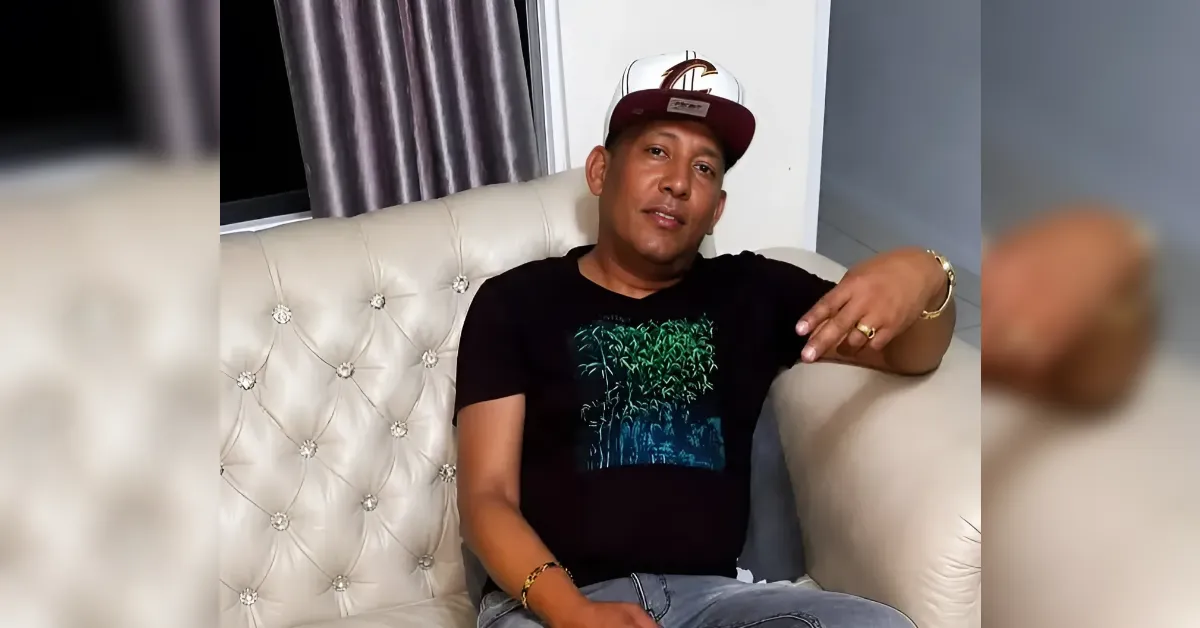 Man in a black graphic t-shirt and maroon cap reclining on a cream tufted sofa, resting his arm on the back.