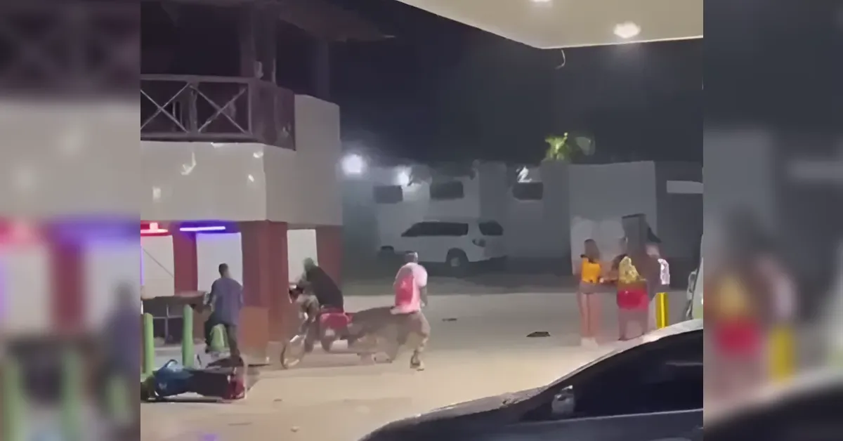 Night scene outside a building with a group of people; a man in pink runs toward a person on the ground while others watch.