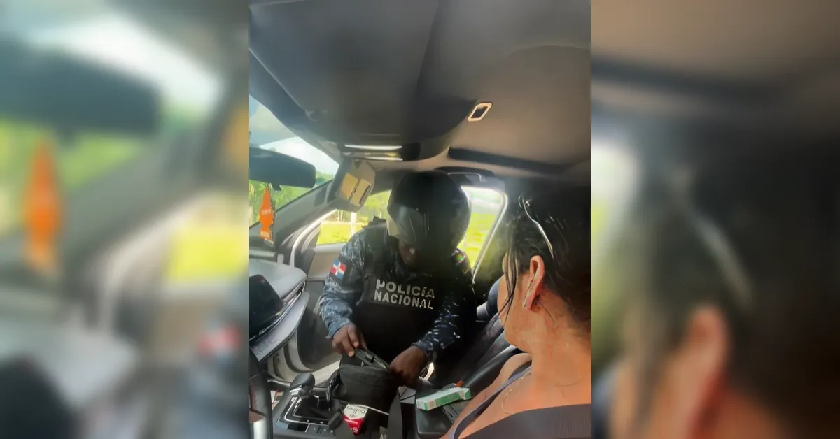 Policía Nacional officer in a helmet seated in the back seat of a car, inspecting gear as a woman in the front passenger seat watches.