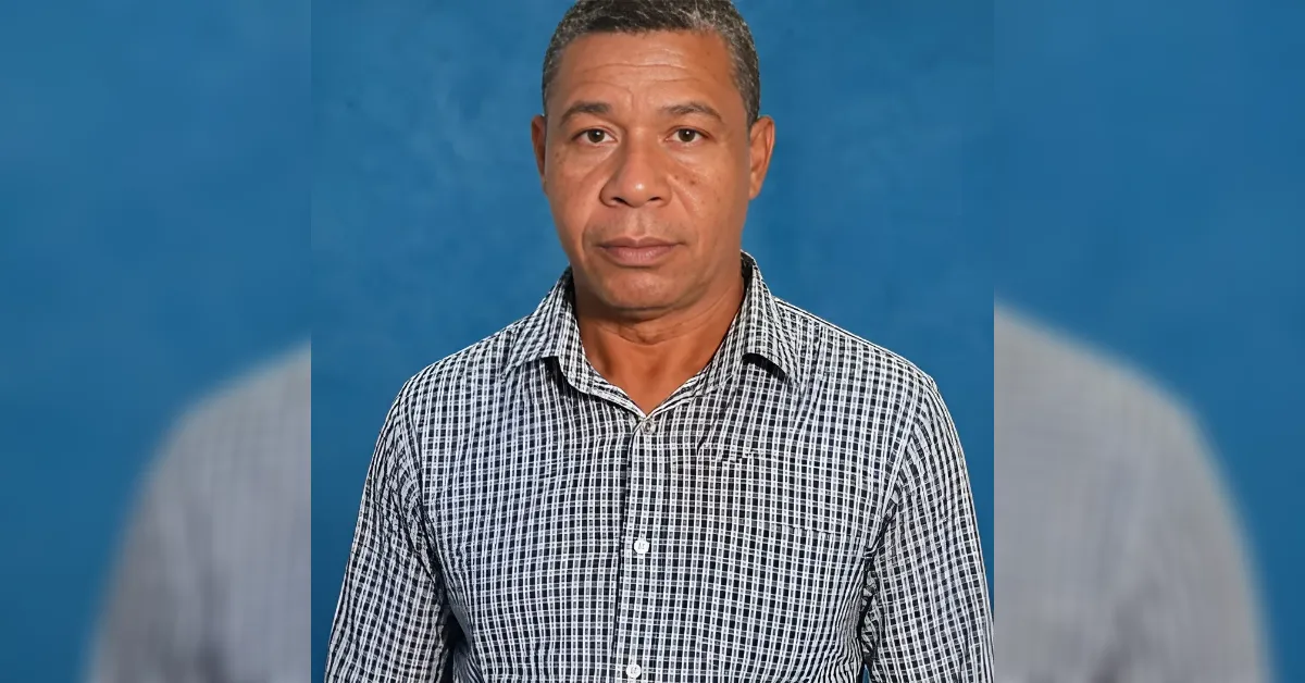 Portrait of a man with short-cropped hair wearing a black-and-white checkered shirt, standing against a blue backdrop.