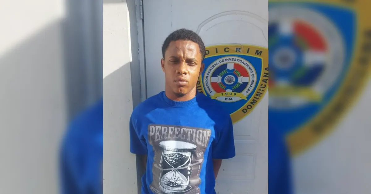 Young man in a blue T-shirt with a 'PERFECTION' graphic, standing against a wall with a police emblem in the background.