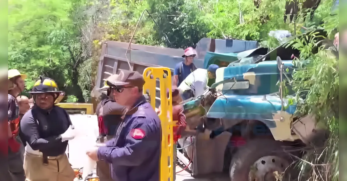 Firefighters and rescue workers assess a crashed blue truck on a sunny roadside.