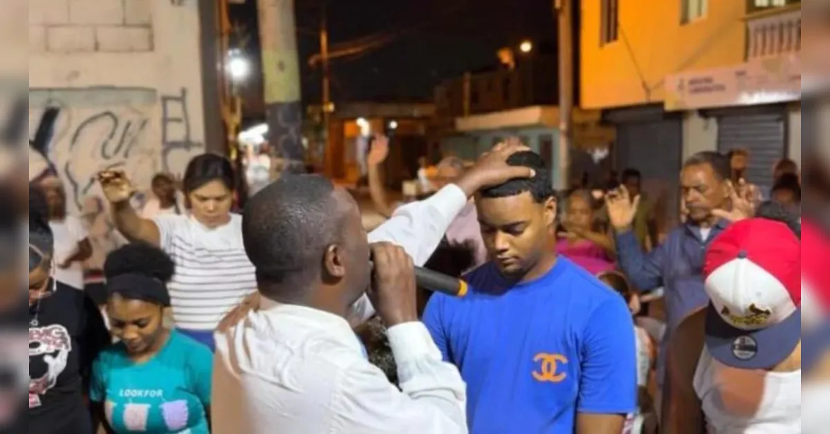 Man with microphone speaks to a man in a blue shirt at a nighttime street gathering.