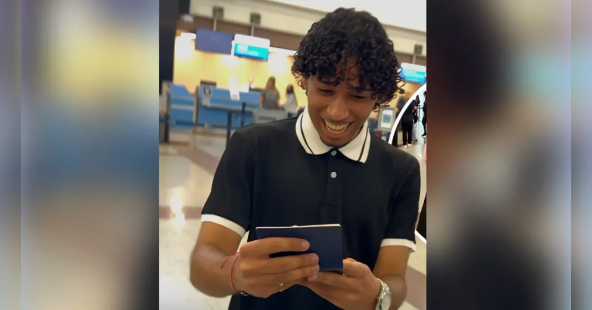 Smiling man in a black polo shirt with white trim using a smartphone in an airport terminal.